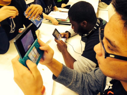 Students play Super Smash Bros against each other on the 3ds as spectators watch from behind, observing their moves and skillsets to bet who will win. 